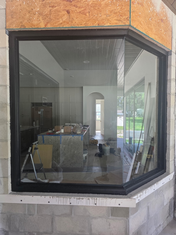 Under-construction kitchen visible through a large bay window, with a worktable, ladder, and assorted tools on the island outside.