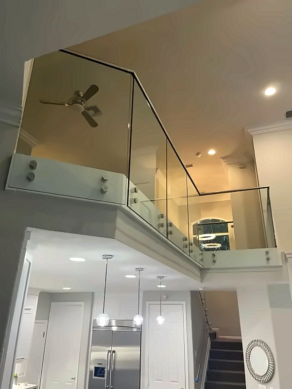 Open-concept interior with a glass railing balcony overlooking a bright kitchen, stainless fridge, and stairs to the right.