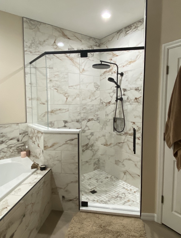 Modern bathroom with a glass-paneled shower enclosure, black metal hardware, and marble-tiled walls and floor; rainfall and handheld showerheads inside the shower