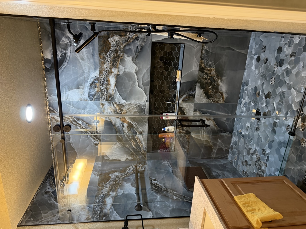 Glass-framed walk-in shower with blue-gray marble walls and a built-in niche of toiletries.|Built-in niche holds shampoo and lotion inside a marble shower enclosure with glass doors