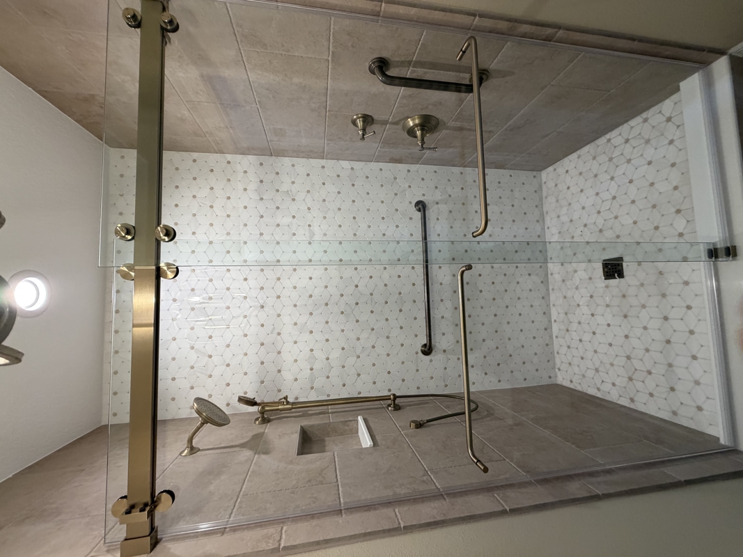 Walk-in glass-front shower with two horizontal grab bars, a handheld showerhead, and built-in niche on tiled walls.